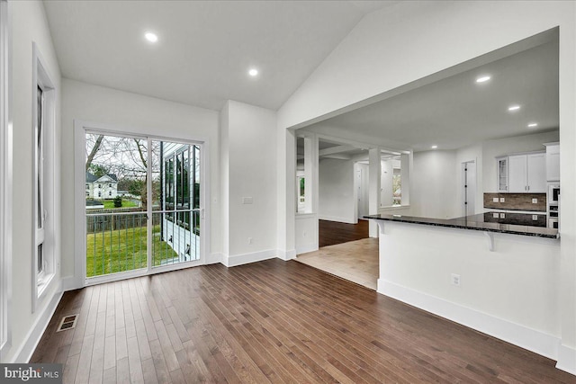 interior space featuring lofted ceiling, dark wood-type flooring, dark stone counters, tasteful backsplash, and white cabinetry