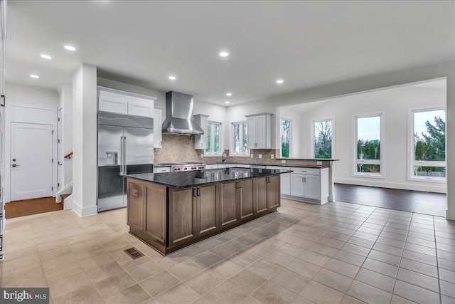 kitchen featuring white cabinetry, built in fridge, a kitchen island, and wall chimney range hood