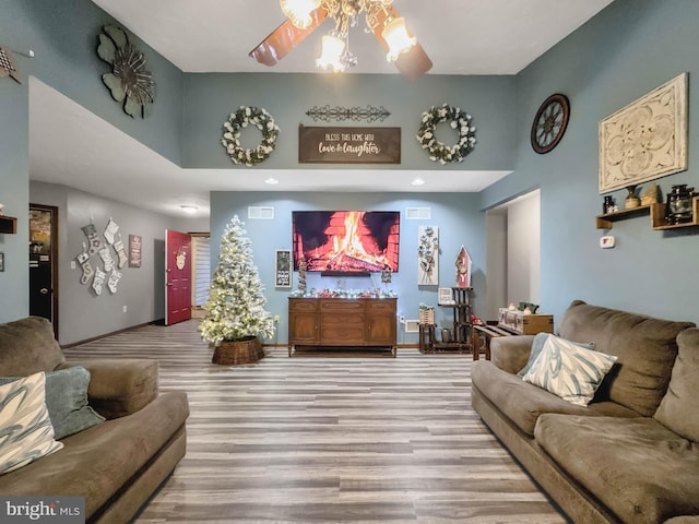 living room featuring ceiling fan, a high ceiling, and light hardwood / wood-style flooring