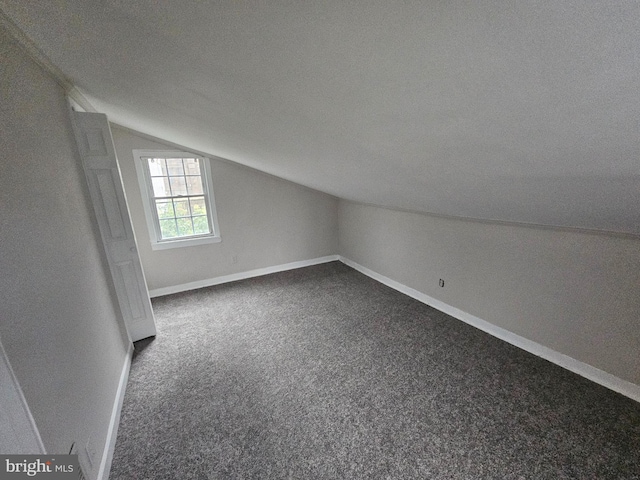 additional living space with a textured ceiling, dark carpet, and lofted ceiling