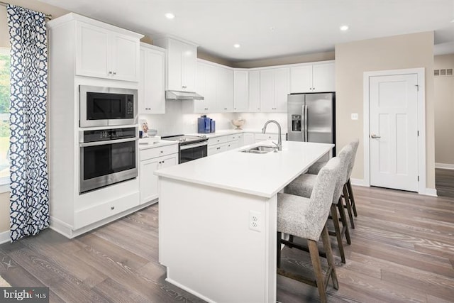 kitchen featuring a center island with sink, sink, a kitchen bar, white cabinetry, and stainless steel appliances