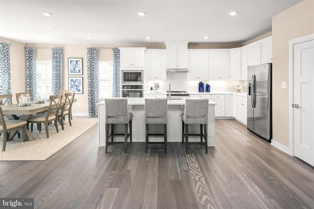 kitchen featuring dark hardwood / wood-style flooring, a breakfast bar, stainless steel appliances, a kitchen island with sink, and white cabinetry