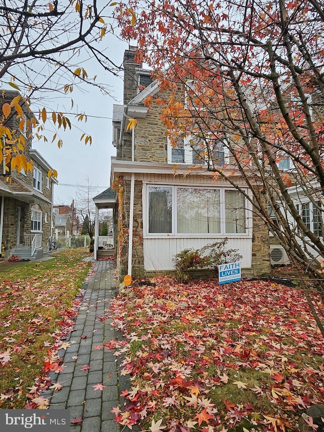 view of property exterior featuring stone siding, a chimney, and ac unit