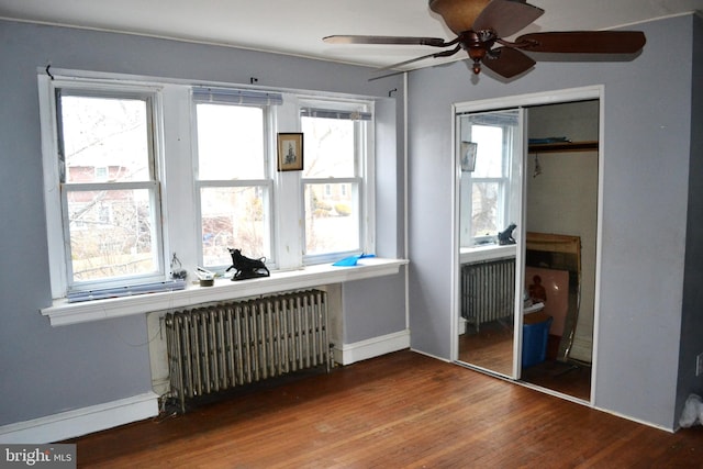 bedroom featuring multiple windows, radiator, wood finished floors, and a closet