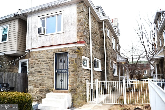 view of property featuring stone siding, cooling unit, and fence