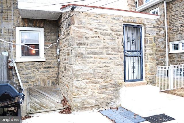 view of exterior entry with stone siding and fence