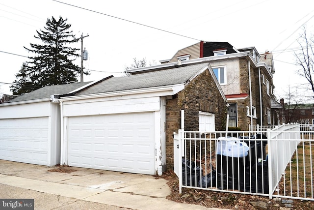 view of home's exterior featuring a garage, stone siding, an outbuilding, and fence