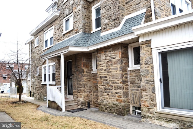 entrance to property with mansard roof, stone siding, and roof with shingles