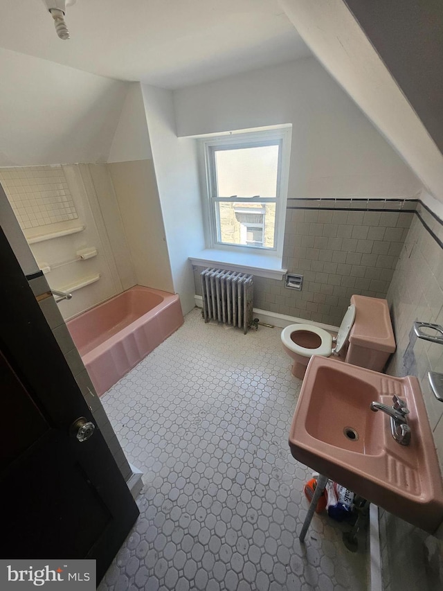 full bathroom featuring a tub, toilet, radiator heating unit, lofted ceiling, and a sink