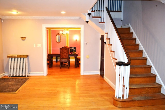 staircase with radiator, ornamental molding, recessed lighting, wood finished floors, and a notable chandelier