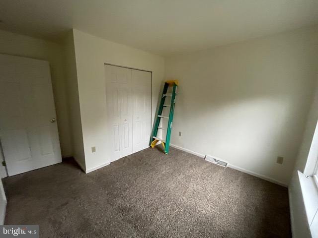 unfurnished bedroom with dark carpet and a closet