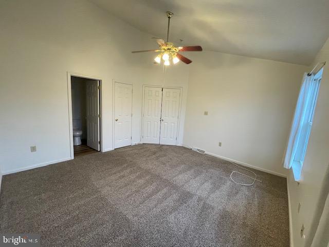 unfurnished bedroom with ensuite bath, ceiling fan, high vaulted ceiling, dark colored carpet, and multiple closets