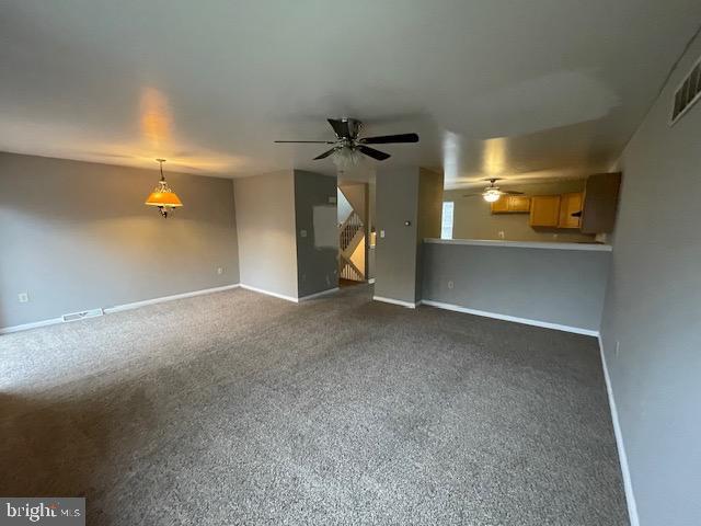 unfurnished living room featuring ceiling fan and dark colored carpet