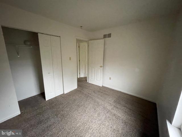 unfurnished bedroom with dark carpet and a closet