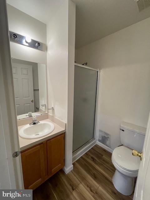 bathroom featuring wood-type flooring, toilet, vanity, and walk in shower