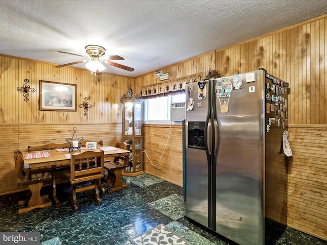 kitchen with stainless steel fridge with ice dispenser, ceiling fan, and wood walls