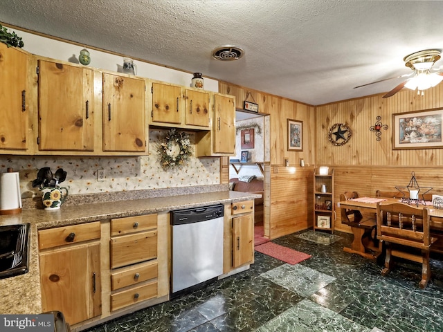 kitchen featuring ceiling fan, sink, stainless steel dishwasher, wood walls, and a textured ceiling