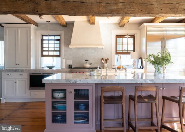 kitchen with light stone countertops, a kitchen breakfast bar, hardwood / wood-style floors, white cabinets, and custom range hood