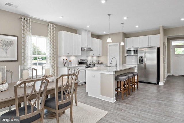 kitchen featuring appliances with stainless steel finishes, pendant lighting, a center island with sink, white cabinets, and light hardwood / wood-style floors