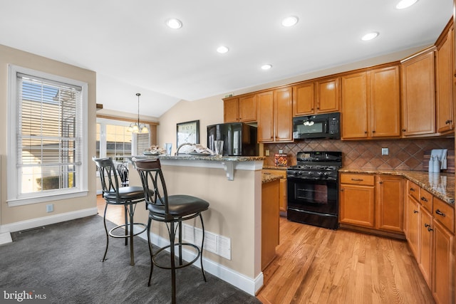 kitchen featuring black appliances, decorative light fixtures, light stone counters, and lofted ceiling