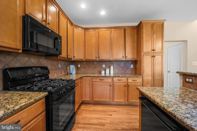 kitchen featuring decorative backsplash, light hardwood / wood-style flooring, black appliances, and stone countertops