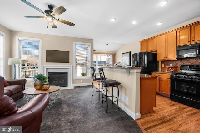 kitchen featuring dark stone countertops, an island with sink, pendant lighting, wood-type flooring, and black appliances