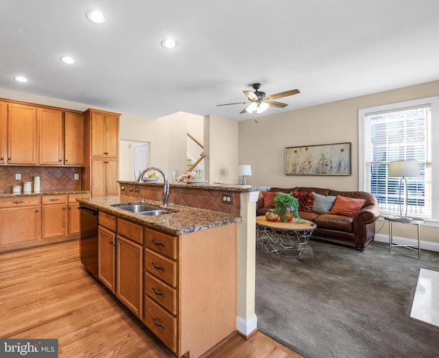 kitchen featuring light wood-type flooring, black dishwasher, an island with sink, and sink