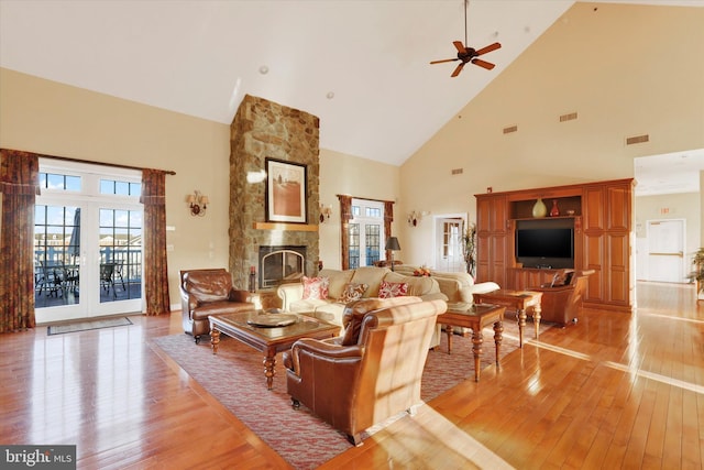 living room with a stone fireplace, ceiling fan, high vaulted ceiling, and light hardwood / wood-style floors