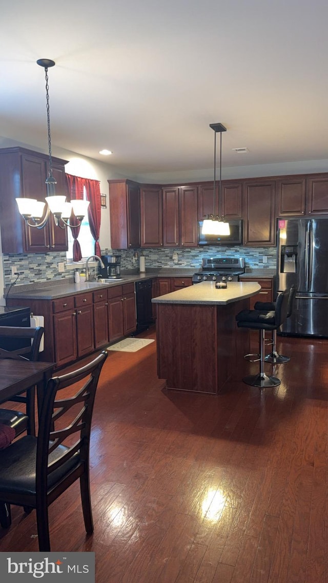 kitchen with hanging light fixtures, appliances with stainless steel finishes, a center island, and sink