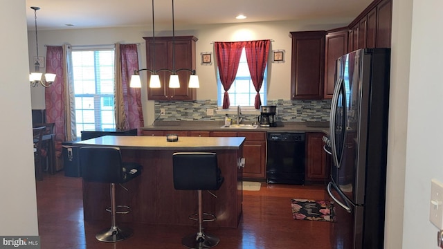 kitchen featuring a kitchen island, sink, a breakfast bar area, hanging light fixtures, and black appliances