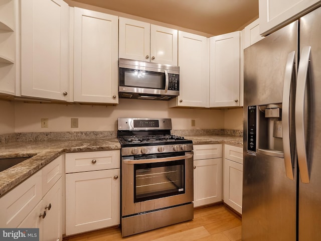 kitchen with light stone counters, white cabinets, light wood-type flooring, and appliances with stainless steel finishes