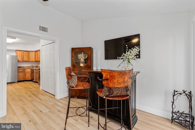 bar featuring stainless steel fridge and light hardwood / wood-style floors