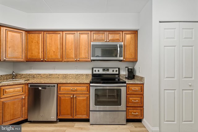 kitchen featuring light stone countertops, appliances with stainless steel finishes, light hardwood / wood-style flooring, and sink