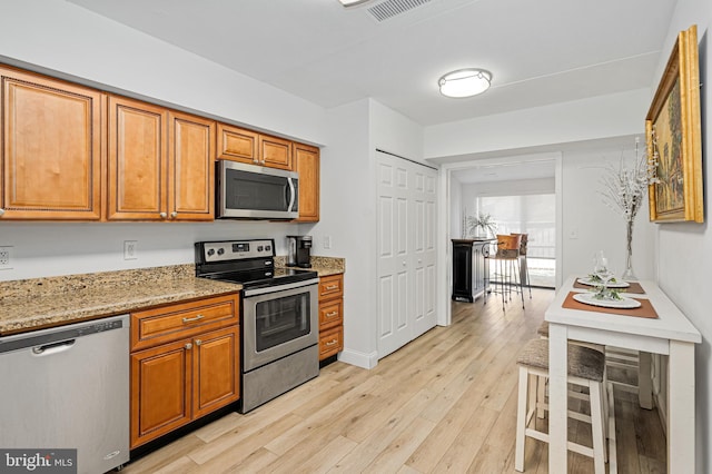 kitchen featuring light stone counters, stainless steel appliances, and light hardwood / wood-style floors