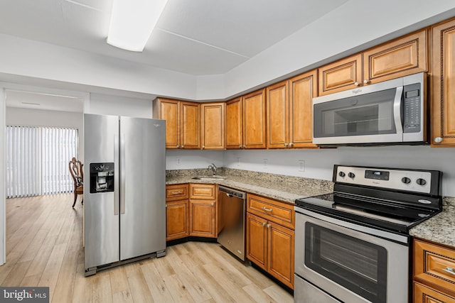 kitchen featuring light stone countertops, sink, light hardwood / wood-style floors, and appliances with stainless steel finishes