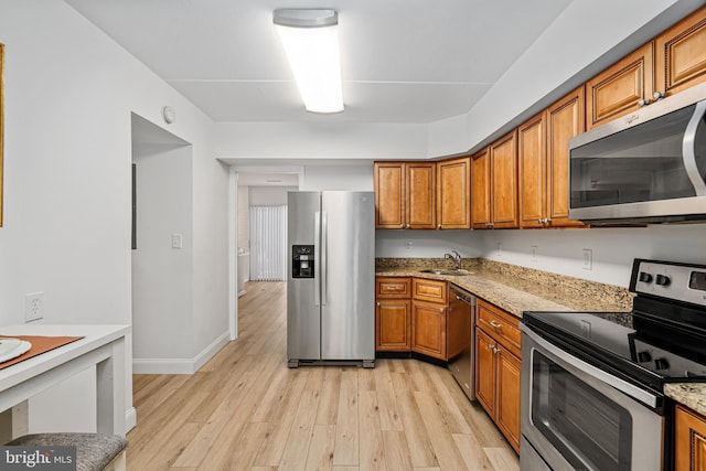 kitchen with appliances with stainless steel finishes, light wood-type flooring, light stone counters, and sink