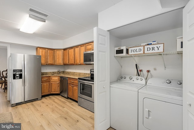 kitchen with sink, washer and clothes dryer, light wood-type flooring, and appliances with stainless steel finishes