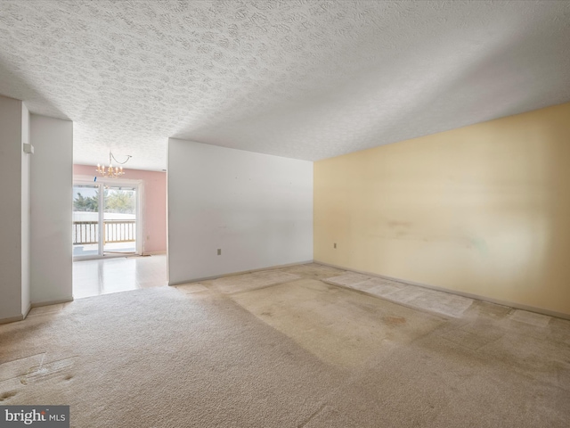 carpeted empty room with a textured ceiling and a notable chandelier