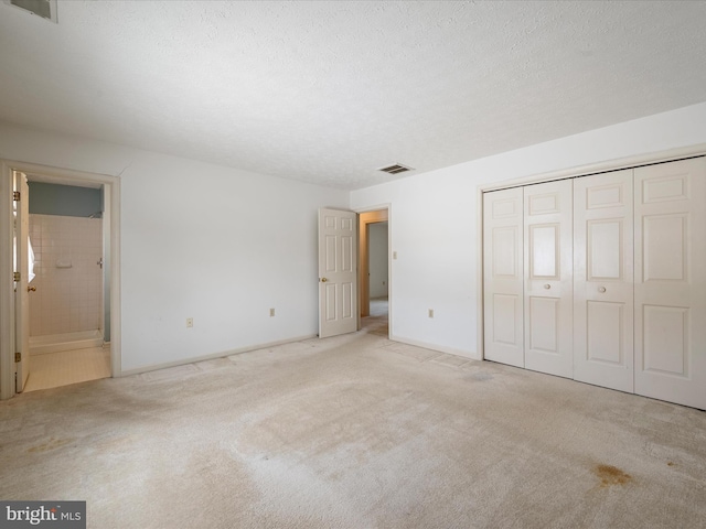 unfurnished bedroom with light carpet, connected bathroom, a closet, and a textured ceiling