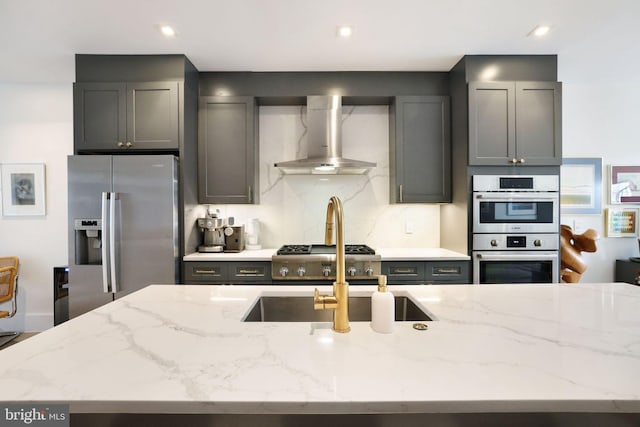 kitchen featuring light stone countertops, stainless steel appliances, gray cabinets, and wall chimney exhaust hood