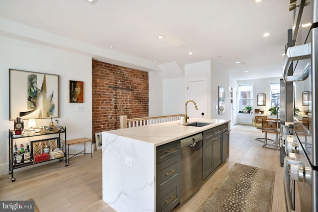 kitchen featuring light stone countertops, light wood-type flooring, stainless steel dishwasher, sink, and an island with sink