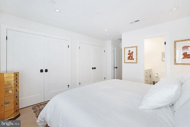 bedroom with ensuite bath, light hardwood / wood-style flooring, and two closets