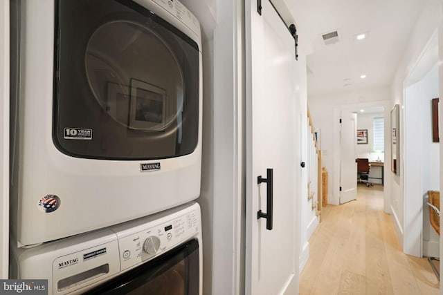 clothes washing area with stacked washer / dryer, light hardwood / wood-style flooring, and a barn door