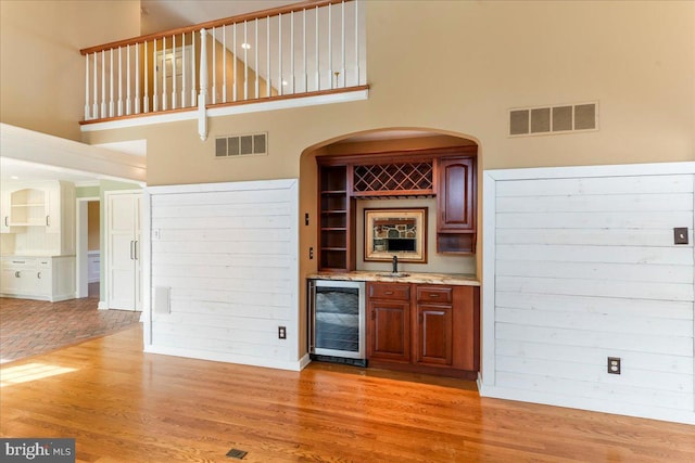 bar featuring wine cooler, a towering ceiling, sink, and light hardwood / wood-style floors