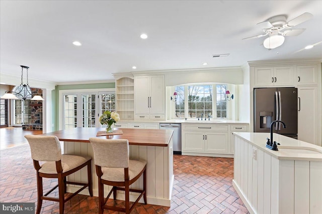 kitchen with white cabinetry, an island with sink, appliances with stainless steel finishes, and ornamental molding