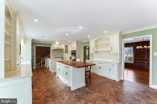 kitchen with crown molding, a breakfast bar, white cabinetry, a center island, and ceiling fan with notable chandelier