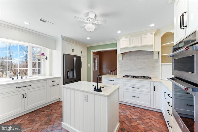 kitchen featuring tasteful backsplash, sink, ornamental molding, stainless steel appliances, and a center island with sink