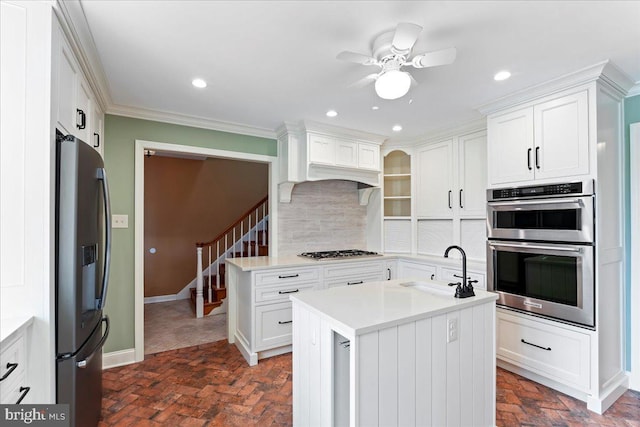 kitchen featuring appliances with stainless steel finishes, white cabinetry, sink, backsplash, and a kitchen island with sink