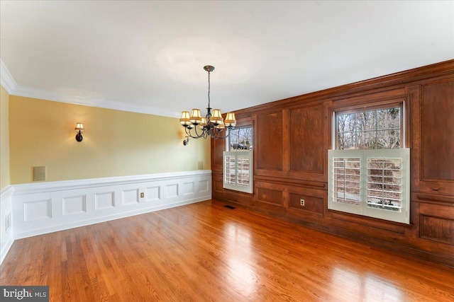 unfurnished dining area with a notable chandelier, crown molding, and light wood-type flooring