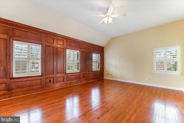 unfurnished room featuring light hardwood / wood-style flooring, wood walls, ceiling fan, and vaulted ceiling